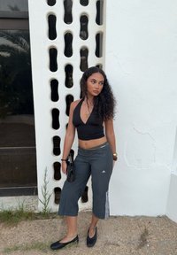 Top corto negro con cuello halter, pantalones cortos grises con tres franjas blancas, zapatos planos negros, combinado con un bolso pequeño y acentos dorados.