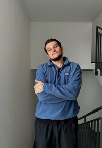 Kék bolyhos pulóver félcipzárral és hímzett logóval, fekete sorttal párosítva. Az anyag lágy kinézetű, kissé texturált felülettel.