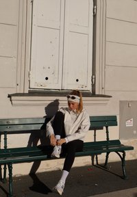 Chaussures de sport gris clair sur une femme assise sur un banc vert, portant une veste blanche et un legging noir, en train de faire ses lacets.