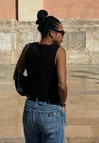 Top nero senza maniche, collo alto, abbinato a jeans a vita alta di un blu chiaro con orli arrotolati e una piccola etichetta nella tasca posteriore.