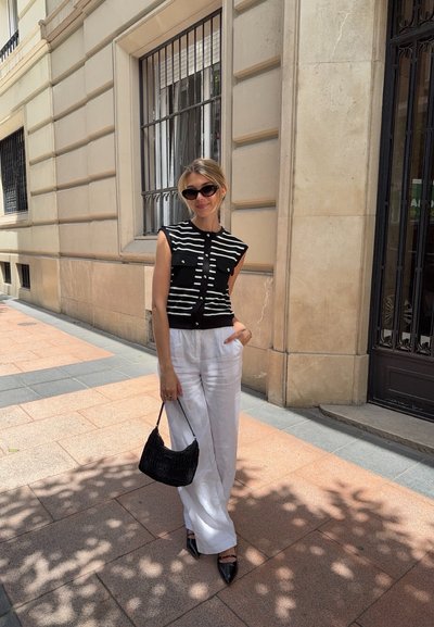 Top sin mangas a rayas en blanco y negro con cierre de botones, combinado con pantalones anchos blancos. Los accesorios incluyen un bolso negro texturizado y tacones negros puntiagudos.