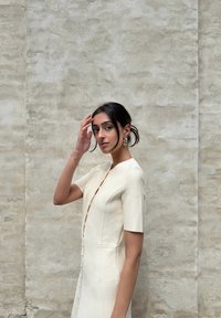 Un vestito color crema con maniche corte, una silhouette aderente e bottoni lungo la parte anteriore. Il tessuto ha una texture delicata.