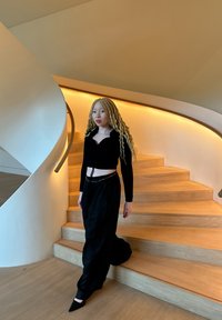 Svart långärmad topp med hjärtformad halsringning, kombinerad med flödande svarta vida byxor. Snygga trätrappor och släta böjda räcken i bakgrunden.