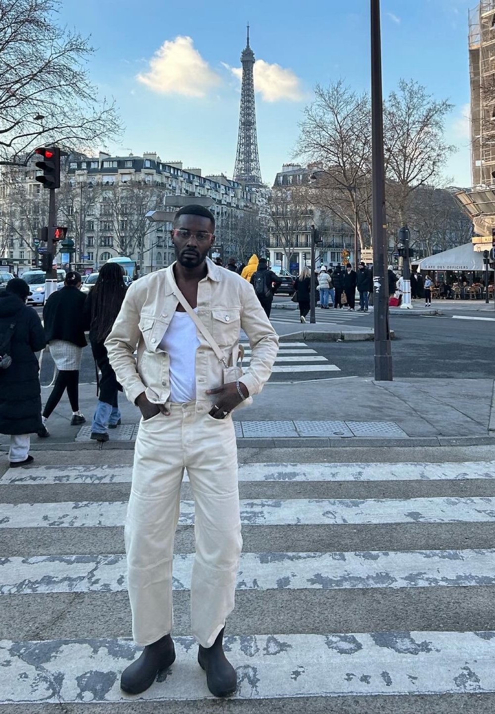 Chaqueta de mezclilla beige y pantalones con una camiseta sin mangas blanca, combinados con botas de goma negras. El fondo presenta la Torre Eiffel y un paisaje urbano.