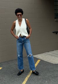 Ανοιχτό κρέμα πλεγμένο γιλέκο με V λαιμόκοψη, συνδυασμένο με ανοιχτό μπλε ψηλόμεσα τζιν με φθορές. Μαύρα παπούτσια και μαύρη τσάντα.