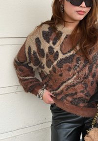 Καστανή και καφέ υπερμεγέθη μπλούζα με λεοπάρ σχέδιο, φτιαγμένη από αφράτο υλικό. Μαύρο δερμάτινο παντελόνι και ασημένια βραχιόλια συμπληρώνουν την εμφάνιση.