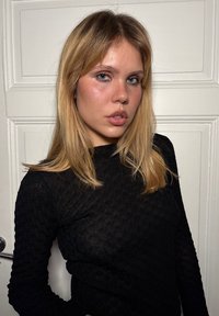 Zwarte langemouwen top met een textuurpatroon, een aansluitend ontwerp en een ronde halslijn, gedragen door een model tegen een witte achtergrond.