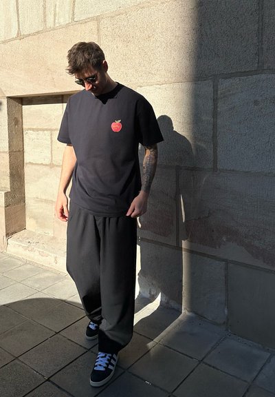 Camiseta negra con un pequeño gráfico de una manzana roja, combinada con pantalones negros holgados y zapatillas negras con acentos blancos.