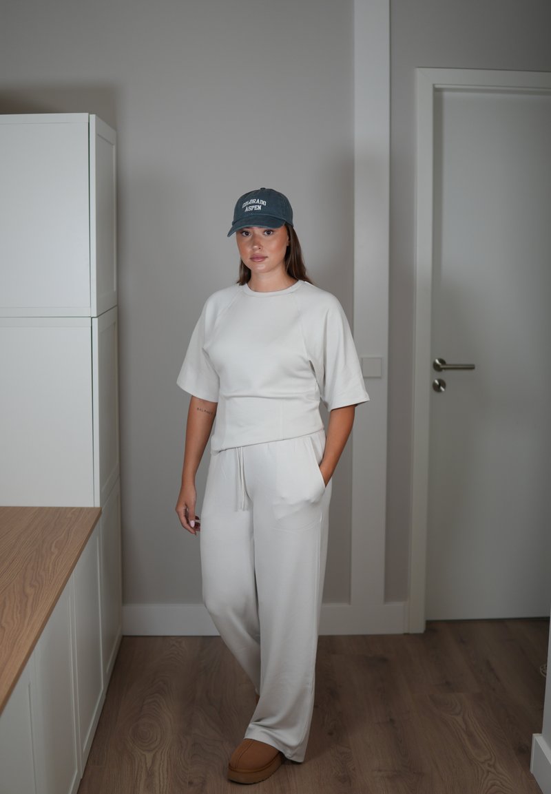 Ensemble de loungewear assorti gris clair comprenant un haut court à manches courtes et un pantalon ample. Texture douce, associé à une casquette foncée et des chaussons.