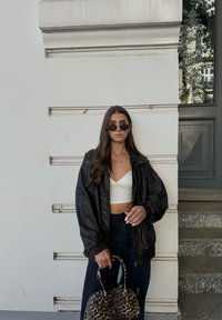Μαύρο δερμάτινο τζάκετ πάνω από ένα λευκό κοντό τοπ, συνδυασμένο με ψηλόμεσα σκούρα τζιν. Κρατά μια τσάντα με λεοπάρ σχεδίαση. Κυκλικά γυαλιά ηλίου.