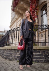 Fekete műbőr zakó és hozzá illő, bőszárú nadrág, piros kézitáskával, amely pöttyös pántokkal rendelkezik, és átlátszó sarkú szandállal párosítva.