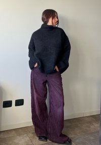 Svart oversized tröja med hög krage, tillsammans med vida lila byxor. Båda plaggen har mjuka texturer och avslappnade passformer.