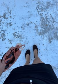 Schwarzer Minirock, dunkelbraune Ballerinas, rosa geflochtene Handtasche mit Sonnenbrille darin. Der Hintergrund zeigt eine strukturierten blauen Oberfläche.