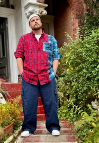 Camisa xadrez em vermelho e azul com um bolso, calças cargo em azul-marinho e ténis brancos, usada com um gorro de malha, em pé em degraus de pedra.