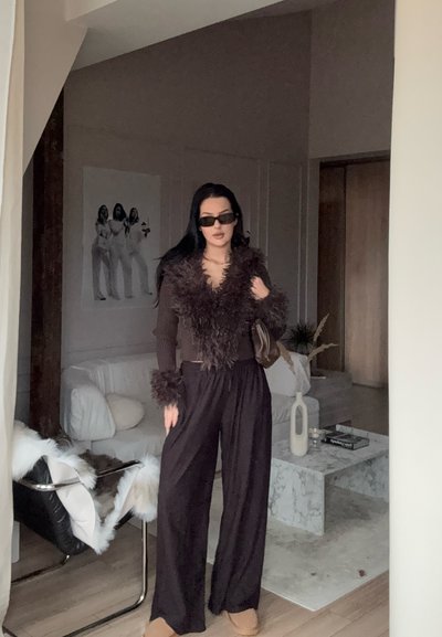 Top marrón acanalado con cuello y puños peludos, combinado con pantalones negros holgados. Gafas de sol negras y un bolso marrón, con un fondo interior minimalista.