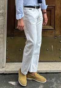 Λευκά τζιν με ίσια γραμμή, συνδυασμένα με ανοιχτό καφέ σουέτ παπούτσια χωρίς κορδόνια. Η μπλούζα είναι ανοιχτό μπλε, με γυρισμένα μανίκια και μια σκούρα ζώνη.