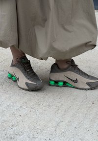 Tan Nike trainers with green cushioning, featuring a textured suede and mesh upper, a black swoosh logo, and a ridged rubber sole.