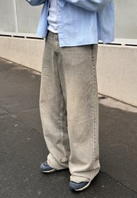 Világoskék, csíkos gombos ing fehér póló fölött; sz�ürke, bőszárú farmer enyhén kopott hatással; sötét cipőt viselnek fehér talppal.