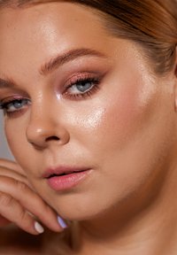 Nærbilde av et ansikt med lys hud, lyseblå øyne, subtil rosa øyenskygge og en naturlig leppefarge. Håret er trukket tilbake, noe som avslører en glatt tekstur.