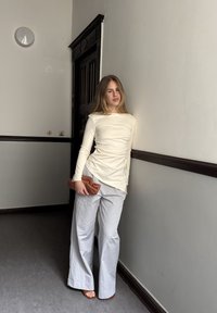 Kreminė ilgomis rankovėmis palaidinė su surinkimo detalėmis, derinama su šviesiai pilkomis plačiomis kelnėmis. Laiko rudą delninę. Sklandžios tekstūros visame. 