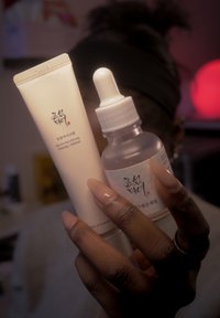 Hudvårdsprodukter: ett vitt rör märkt "Revive Eye Serum" med vridkork och en klar glasdroppeflaska med vit etikett.