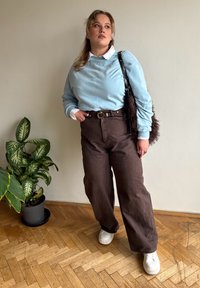 Helehall sinine jakk, all valge kraega särk, tumepruunid laiad püksid, valged tennised, tume karvane käekott. Siseruumides.