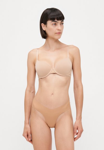 Sostén acolchado beis con tirantes ajustables, diseño sin costuras; bragitas nude de corte alto a juego con textura suave. Ambos presentan un estilo minimalista.