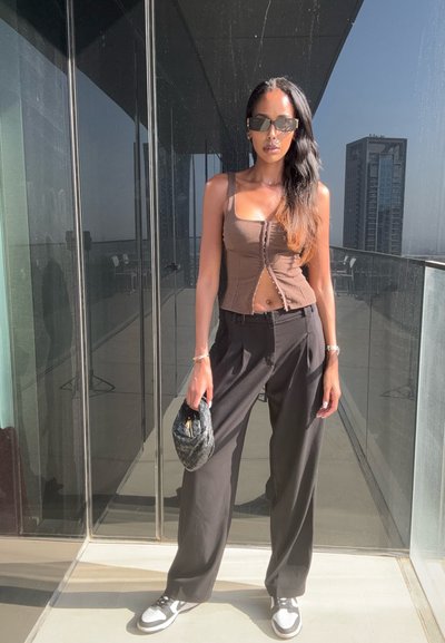 Top corto de canalé marrón con detalle de botones en el frontal, combinado con pantalones anchos negros y zapatillas blancas. Sosteniendo un pequeño bolso negro texturizado.