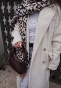 Manteau de couleur crème avec des boutons ronds, assorti à une écharpe imprimée léopard et un sac à main marron foncé. Comprend un collier de perles et des bagues en argent.