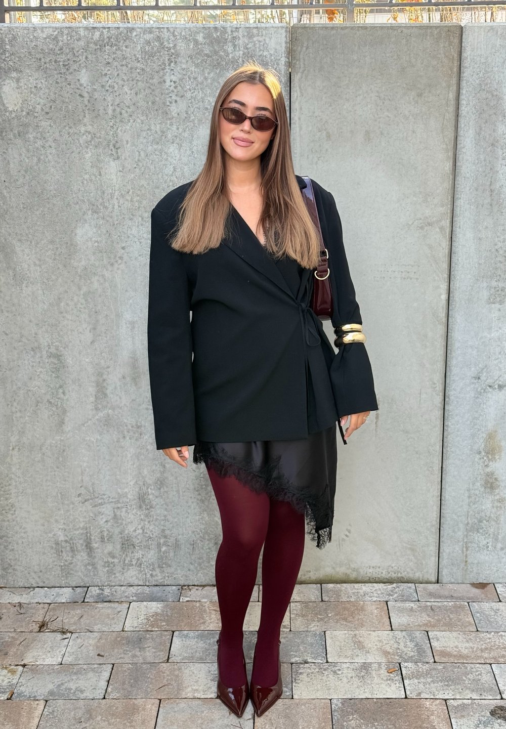 Melns blazera jakas ar garām piedurknēm, caurspīdīga melna svārku ar mežģīņu apakšu, bordo krāsas zeķubikses un tumši sarkanas pulētas augstpapēžu kurpes. Aksesuārs ir zelta aproce.