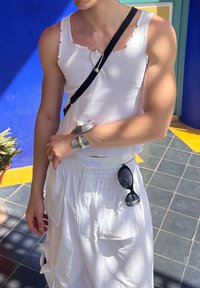 Top de tirantes blanco con textura acanalada y bordes deshilachados, combinado con pantalones cortos cargo blancos. Una pulsera de plata y gafas de sol negras complementan el conjunto.