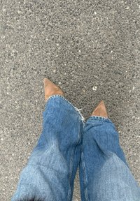 Escarpins marron à bout pointu associés à un jean flare bleu à ourlet effiloché, avec une surface d'asphalte texturée visible en dessous.