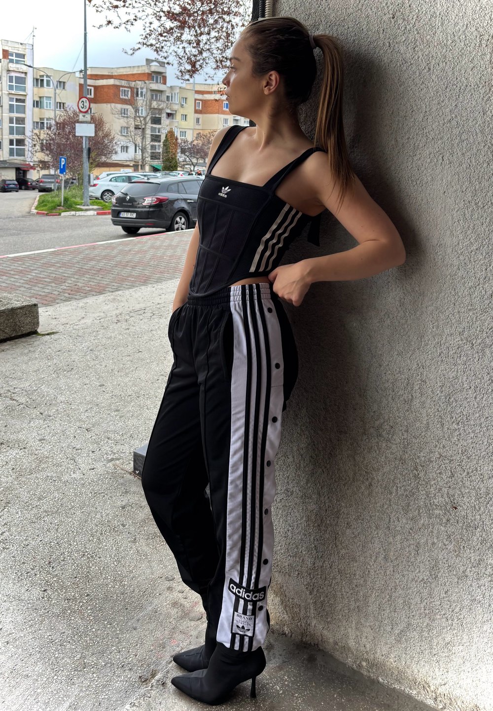 Fekete, testhez simuló felső vastag pántokkal és Adidas logóval, fekete-fehér, patentos sportnadrággal párosítva. A szettet fekete tűsarokkal egészítjük ki.