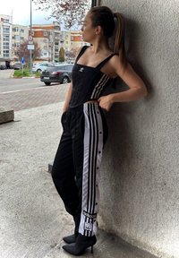 Fekete, testhez simuló felső vastag pántokkal és Adidas logóval, fekete-fehér, patentos sportnadrággal párosítva. A szettet fekete tűsarokkal egészítjük ki.