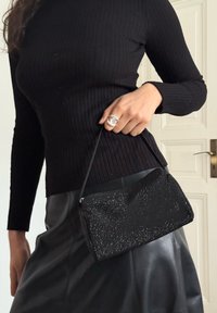 Pochette noire ornée de perles avec une fermeture éclair, dotée d'une surface texturée et d'une sangle fine. Assortie à un haut noir côtelé et une jupe en cuir.