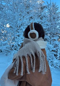 Cotițe din blană artificială maro cu căptușeală albă, purtate cu o eșarfă bej cu franjuri. Fundalul include copaci acoperiți cu zăpadă.