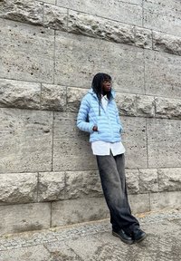 Šviesiai mėlynas pūkinis švarkas su gobtuvu ir horizontaliomis siūlėmis. Derinamas su balta marškinių apykakle ir juodomis plačiomis kelnėmis. Tamsūs batai.