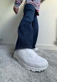 Hvide Nike Air Max sneakers med tekstureret mesh og læderoverdel, der har en synlig Air-enhed og snøresystem, parret med mørkeblå jeans.