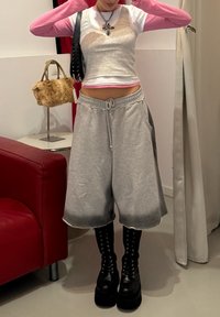 Hallid, üle mõõdu suured püksid, millel on järkjärguline haihtumise efekt, koos lühikese halli tankitopiga ja allpool roosa pika varrukaga särgiga. Mustad platvormsaapad.