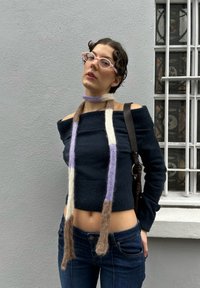 Σκούρο μπλε off-shoulder πουλόβερ, εφαρμοστό, με υφή. Μακρύ, πολύχρωμο μάλλινο κασκόλ κρέμεται από τον λαιμό. Σφιχτά τζιν με μέση μέτριου ύψους.