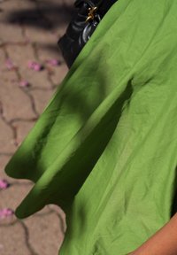 Un tissu vert se drape en plis, présentant une texture lisse et une teinte vive. Un petit sac noir est partiellement visible à côté.
