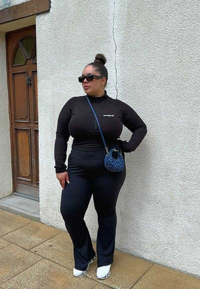 Top negro de manga larga con cremallera, leggings negros acampanados y zapatillas blancas. Acentuado con un bolso de mano azul estampado y gafas de sol oscuras.
