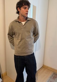 Polo à manches longues gris clair avec col et boutons, associé à un jean bleu foncé. Coupe décontractée avec une texture lisse.