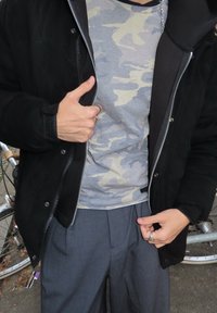 Juoda striukė su užtrauktuku, pilkas kamufliažinis marškinėlis, tamsiai pilkos klostuotos kelnės. Išskirtiniai detalės yra nykščio gestas ir sidabriniai žiedai ant pirštų.