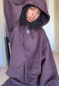 Sudadera oversized marrón con capucha ajustable. Presenta el logo de Adidas en el pecho. Tejido suave y texturizado con un corte relajado.