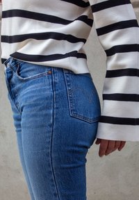 Jeans de denim azul con un ajuste clásico, que presentan un diseño de bolsillo trasero y un desvanecimiento sutil; combinados con un suéter de rayas en blanco y negro.