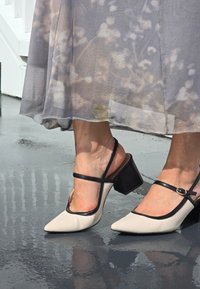 Dvojfarebné béžovo-čierne sandále na podpätku so špičatými špičkami, hrubými blokovými podpätkami a detailmi na remienku. Hladká textúra a minimalistické doplnky.