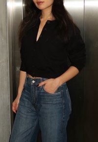 Black cropped cardigan with button closure, matched with high-waisted blue denim jeans that have front pockets and a relaxed fit.