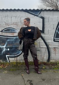 Μαύρο κορμάκι με κενό, καφέ ψεύτικη γούνα, καφέ δερμάτινα παντελόνια και μπορντό τακούνια με μαύρη τσάντα με λευκές βούλες.