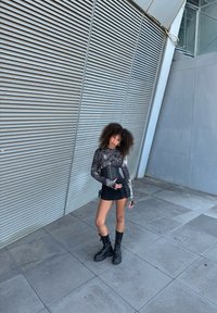 Mini gonna nera con dettagli in pizzo, top a maniche lunghe con fantasia, stivali neri chunky e borsa a tracolla piccola; sfondo testurizzato.